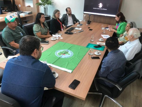 A foto mostra as pessoas que participaram da reunião sentados em volta de uma mesa retangular